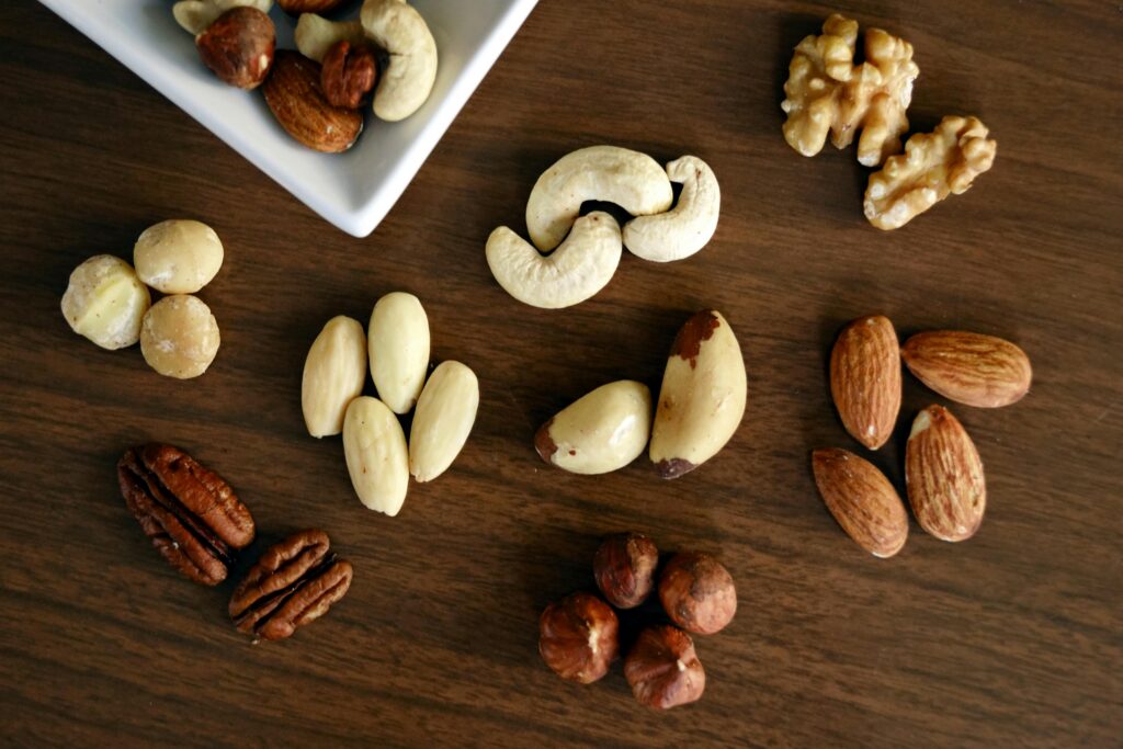 Verschiedene Nüsse auf Holztisch arrangiert – Mandeln, Cashews, Haselnüsse, Walnüsse, Pekannüsse, Macadamianüsse und Paranüsse, teils in einer kleinen Schale.