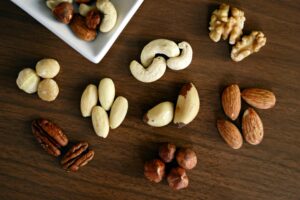 Verschiedene Nüsse auf Holztisch arrangiert – Mandeln, Cashews, Haselnüsse, Walnüsse, Pekannüsse, Macadamianüsse und Paranüsse, teils in einer kleinen Schale.